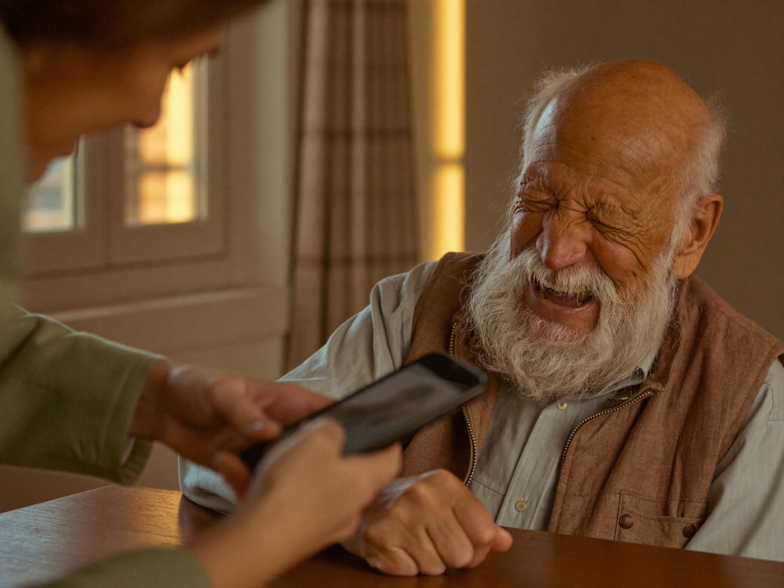 Un signore anziano ride di gusto guardando lo smartphone insieme all'accompagnatrice