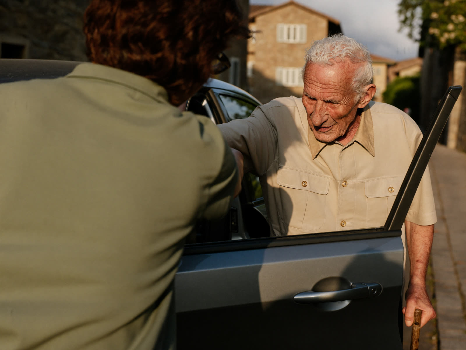 Un'accompagnatrice aiuta un signore anziano a salire in auto in un paese ticinese