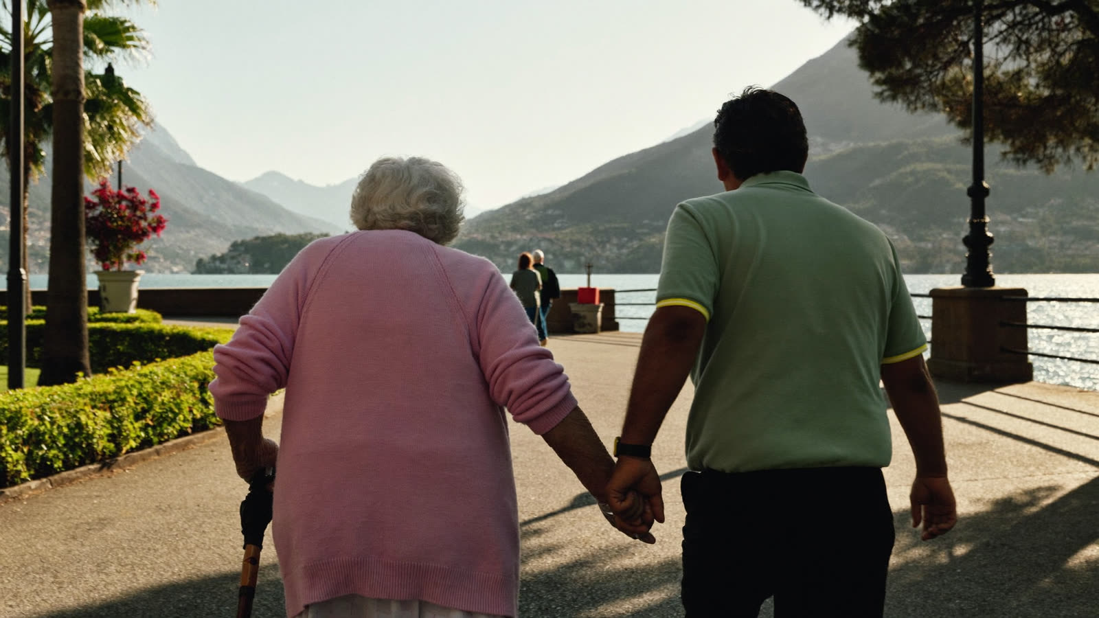 Una signora anziana passeggia mano nella mano con l'accompagnatore sul lungolago di Lugano